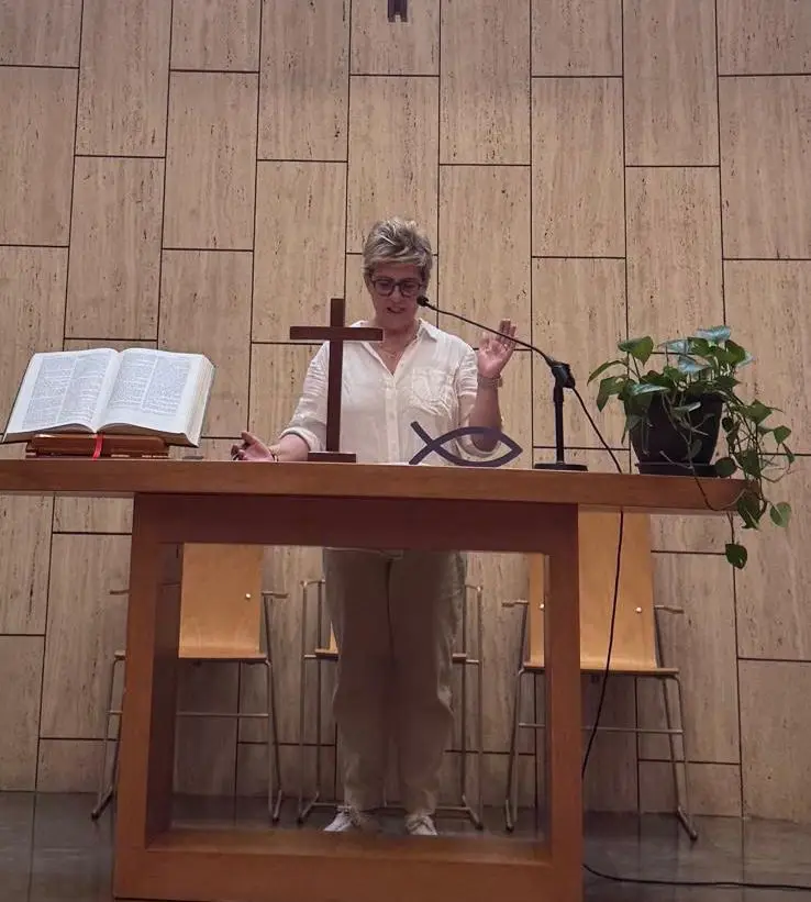 Miembro de la comunidad participando en el culto de la Església Protestant Sant Pau, con la Biblia abierta y la cruz al fondo.